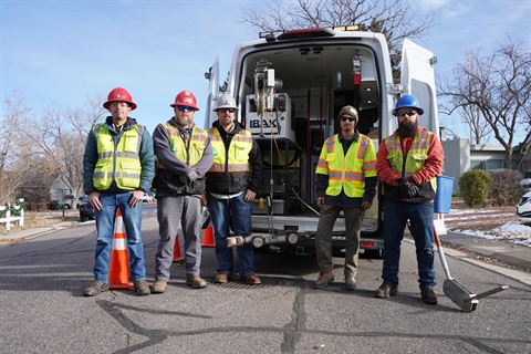 five men standing behind a white van with yellow vests on