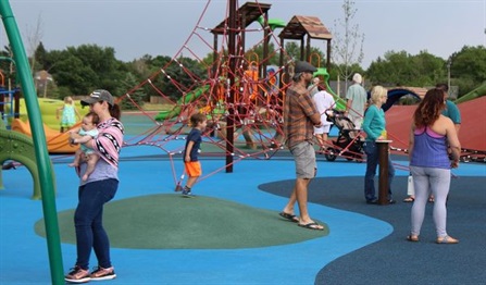 Adults and children walking around enjoying play structures and other features at Carmody Park playground