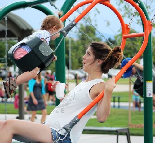 Smiling woman and infant enjoy swinging together on an orange two-person combination swing