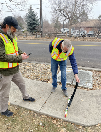 two men in yellow vests measuring a sidewalk