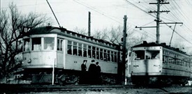 historic black and white of a trolley with three people standing in front of it